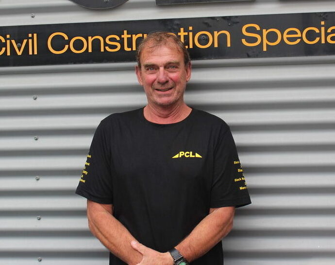 a person wearing a black pcl t shirt stands in front of a corrugated metal wall with a sign reading "civil construction specialist.