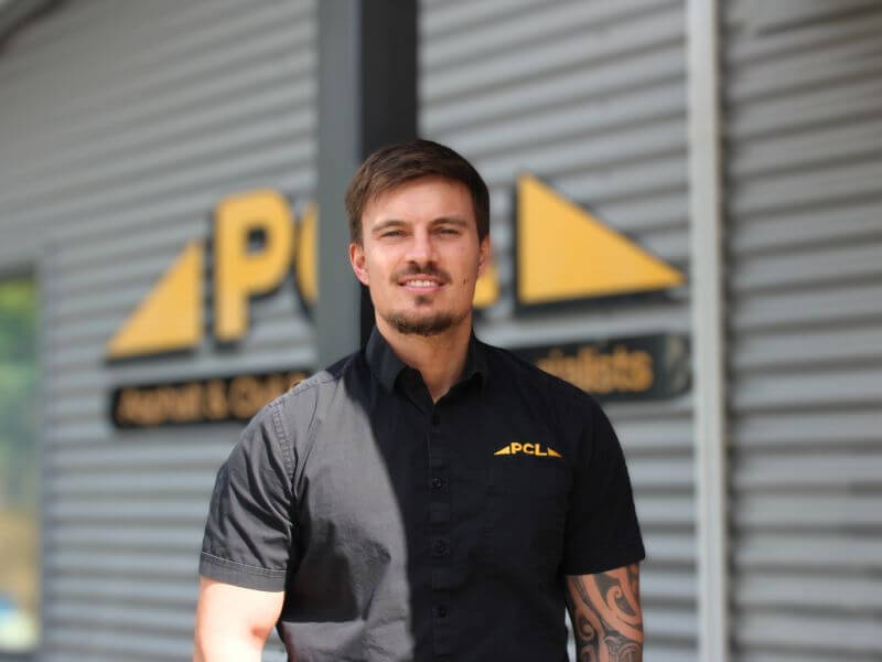 a man in a black collared shirt with a "pcl" logo stands in front of a building with a "pcl" sign.