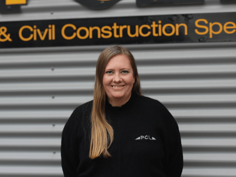 a person with long hair wearing a black pcl sweatshirt stands in front of a sign with "civil construction" visible in the background.