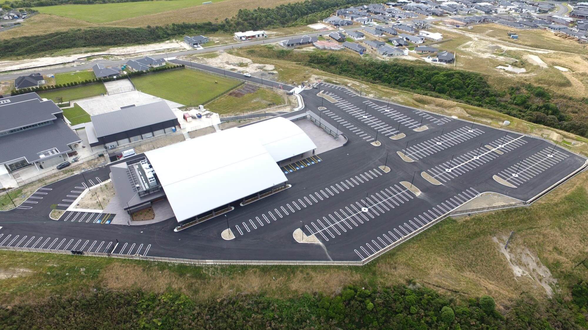 aerial view of a large, newly constructed parking lot adjacent to modern buildings and partially developed surrounding areas.