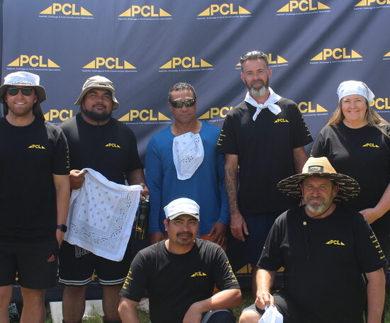 eight people pose in front of a pcl branded backdrop outdoors, wearing mostly black pcl shirts and hats, with tents and trees visible in the background.